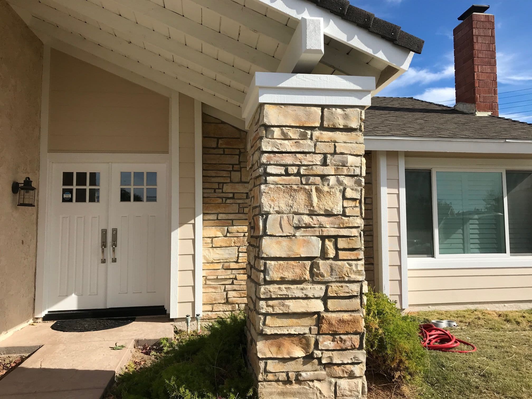Modern home entrance with stone column, double doors, and large window under blue sky.