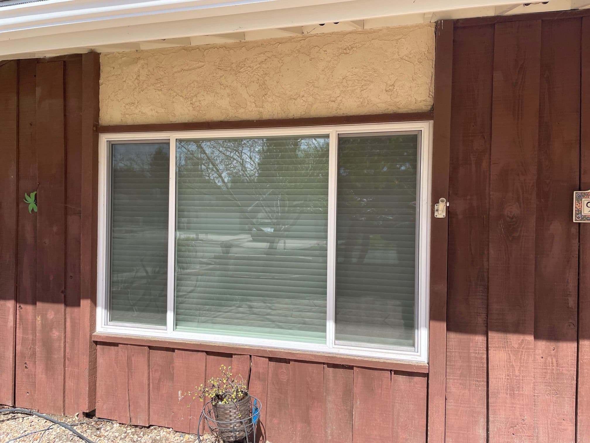 Large three-panel sliding window on a wooden exterior wall with green plants.