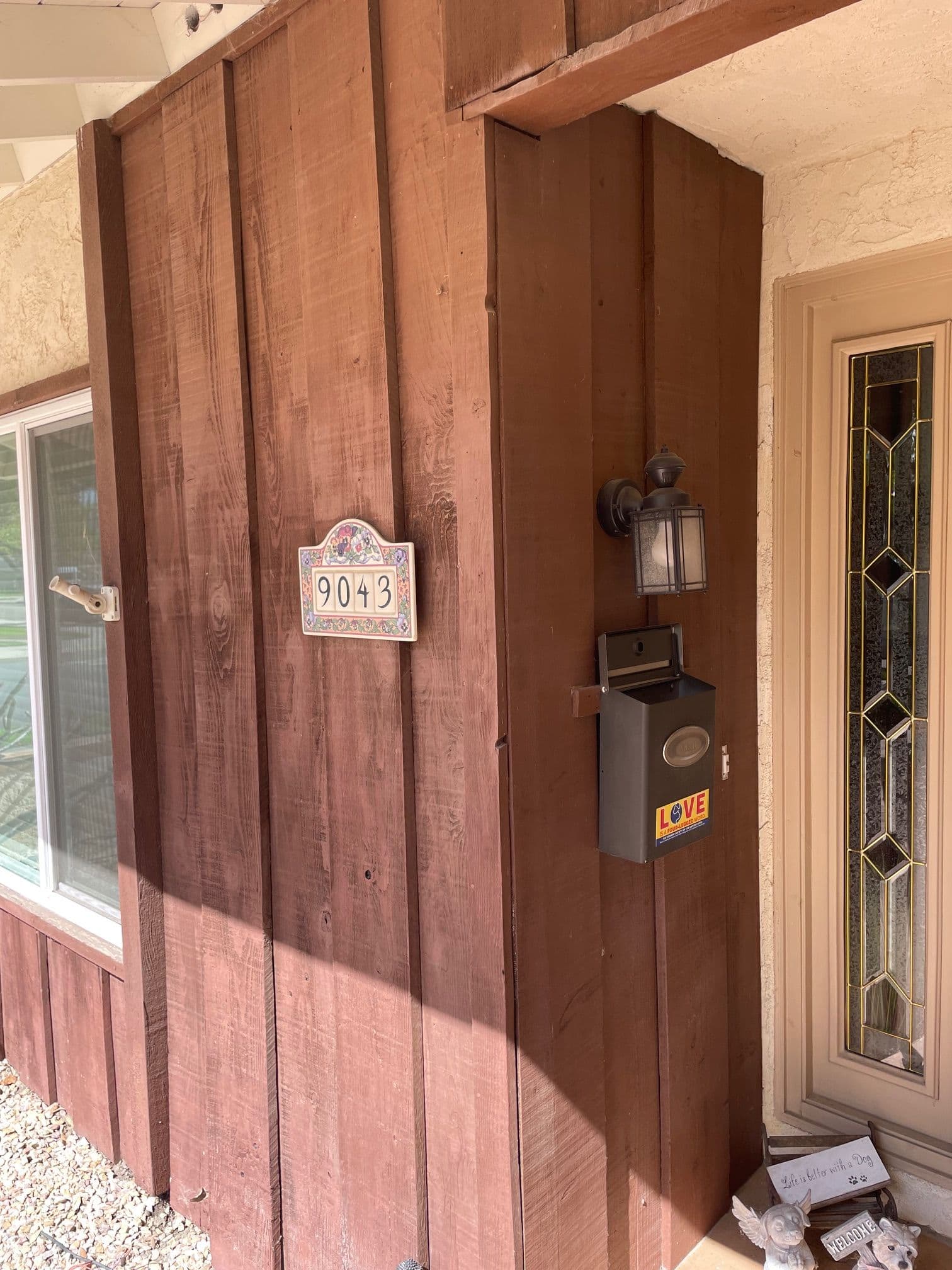 Wooden exterior of a house featuring a mailbox, house number 9043, and decorative lantern.