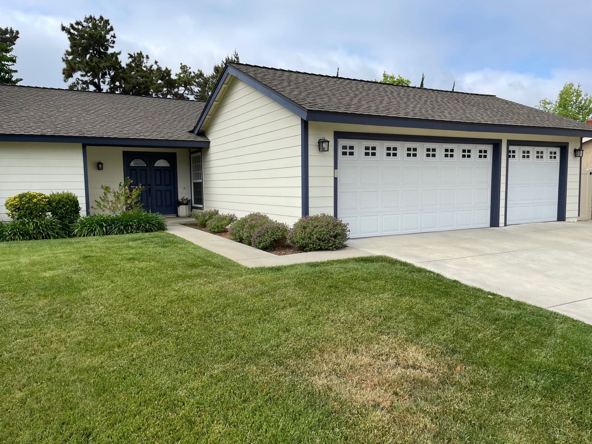 Modern suburban home with a two-car garage, green lawn, and vibrant landscaping.